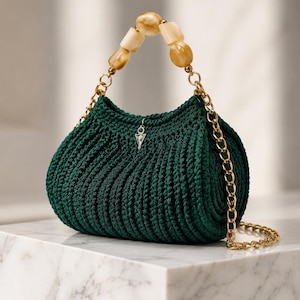 May include: A dark green crochet handbag with a gold chain strap and a beaded handle. The bag has a rounded shape and a small charm hanging from the top. The handle features cream and brown colored beads.