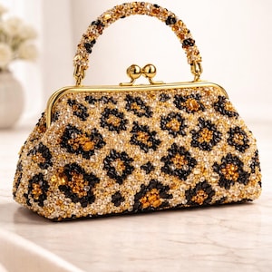 May include: A beaded handbag with a gold frame and handle. The bag features a leopard print design in black, gold, and clear beads. The handle is also adorned with beads. The clasp is gold.