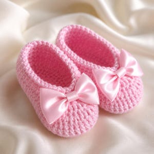 May include: A pair of pink crocheted baby booties with satin bows. The soft pink shoes are displayed on a white satin surface. The bows are a matching pink color.
