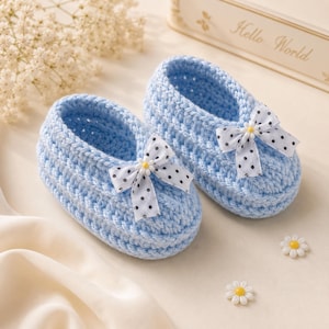 May include: A pair of light blue crochet baby shoes. Each shoe has a white bow with black polka dots and a small yellow flower in the center. The shoes are approximately 4 inches long.