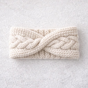 Könnte beinhalten: Cremefarbenes Stirnband aus Strick mit Zopfmuster. Das Stirnband besteht aus weichem, strukturiertem Garn und eignet sich für kaltes Wetter. Das Zopfmuster verleiht dem Accessoire ein dekoratives Element.
