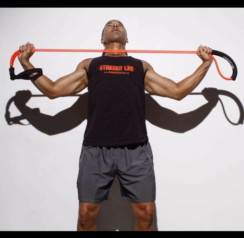 May include: A person is using a resistance band to exercise. The band is orange and has a black handle. The person is wearing a black tank top with the text "STRAIGHT LINE" and gray shorts.