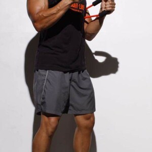 May include: A man wearing a black tank top with the text "Fight Like" on it, gray shorts, and black sneakers. He is holding a red and black resistance band in his hands.