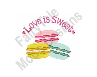 May include: Three colorful macarons with the text "Love is Sweet" in pink lettering and pink hearts on either side of the text.
