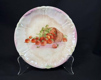 May include: A decorative plate with a hand-painted design of strawberries spilling from a woven basket. The plate has a scalloped edge with a pink and green border. The strawberries are red with green leaves.