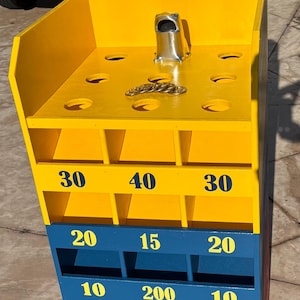 May include: A yellow, blue, and red wooden game board featuring the word COLOMBIA at the top. The board has a metal frog figure, multiple circular holes, and scoring compartments labeled with the numbers 10, 15, 20, 30, 40, and 200.