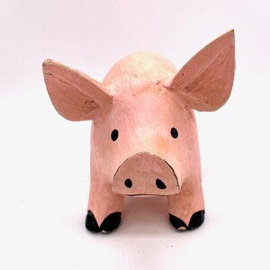 May include: A pink pig figurine with black eyes and a black snout. The pig has floppy ears and black hooves.