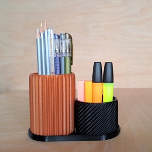 May include: A brown and black desk organiser with a striped pattern holds pencils, pens and highlighters. The organiser has two compartments, one for writing utensils and one for markers.