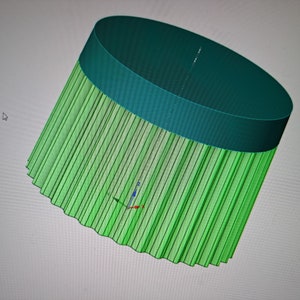May include: A 3D model of a green and teal lampshade with a fluted design. The lampshade is tilted to the side.