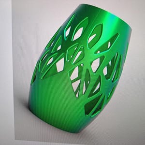 May include: A green, decorative, openwork vase with a geometric pattern. The vase is made of a smooth, shiny material.