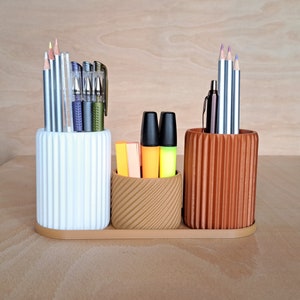 May include: A white and brown desk organiser with three compartments. The compartments hold pencils, pens and markers. The organiser has a striped pattern.
