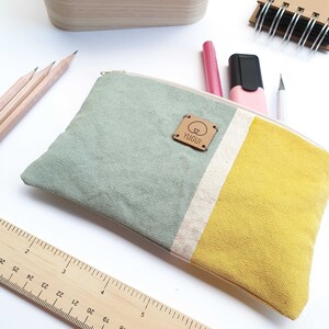 May include: A green, white, and yellow striped canvas pencil case with a brown leather tag that says "YUGUI".