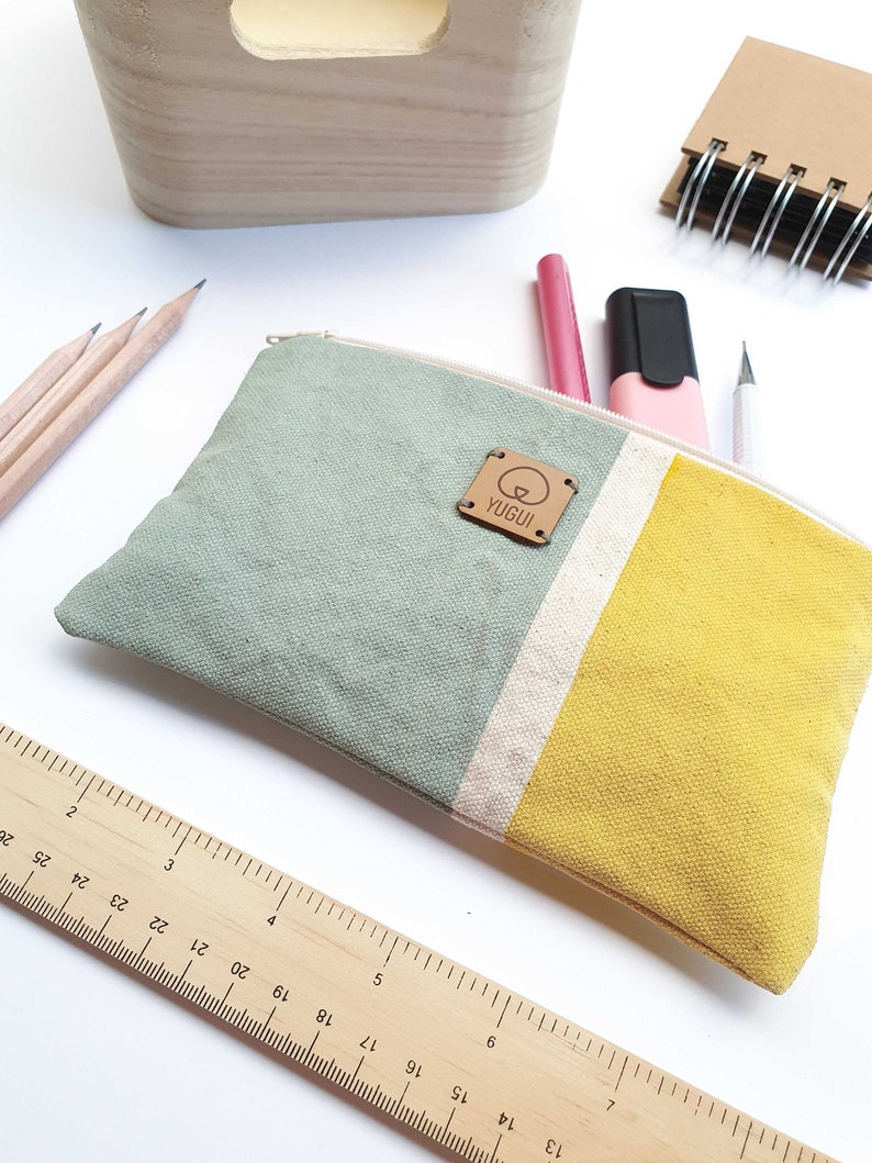 May include: A green, white, and yellow striped canvas pencil case with a brown leather tag that says "YUGUI".