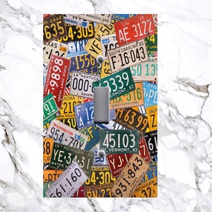 May include: A light switch cover featuring a collage of vintage license plates from different states. The plates are in various colors and feature different numbers and letters. The switch cover is a great way to add a touch of Americana to your home.