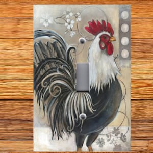 May include: A light switch cover featuring a painting of a black and white rooster with a red comb and wattle. The rooster is surrounded by white flowers and a light brown background.