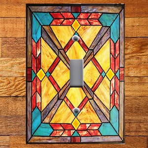 May include: A light switch cover with a stained glass design featuring geometric shapes in shades of red, yellow, blue, and brown.