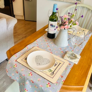 May include: A table setting with a floral tablecloth, a white plate with a heart design, a bottle of wine, a glass of wine, and a vase of flowers. The vase is labelled "Flower Garden".