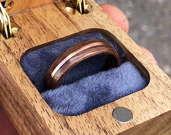 May include: A wooden ring box with a blue velvet interior. A wooden ring with a copper band is inside the box.