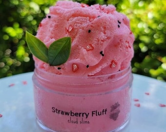 Puede incluir: Un tarro transparente de slime de nube de fresa rosa con chispas negras y rojas. El tarro tiene una etiqueta que dice "Strawberry Fluff cloud slime".