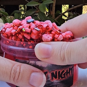 May include: A red slime with red and gold glitter in a clear plastic container with a black and red label that says "Fright Night".