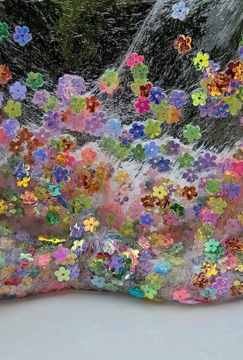May include: Clear slime with iridescent flower-shaped glitter. The slime is a light pink colour and the glitter is a mix of colours, including pink, blue, green, and gold.