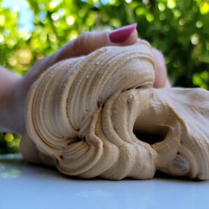 以下が含まれることがあります： 手の中に置かれた、薄い茶色でクリーミーな質感の粘土のクローズアップ。粘土は伸ばされ、様々な形に成形されています。