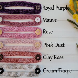 Op de afbeelding: Zes gehaakte gezichtsmasker-verlengstukken in verschillende tinten roze, paars en cr&egrave;me. De kleuren zijn gelabeld met "Royal Purple", "Mauve", "Rose", "Pink Dust", "Clay Rose" en "Cream Taupe".