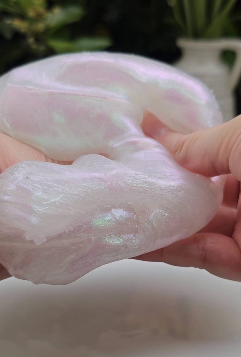 Op de afbeelding: Een close-up van een witte slijm met een iriserende glans. De slijm wordt in een hand gehouden en is zacht en kleverig.