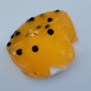 K&ouml;nnte beinhalten: Eine gelbe Passionsfrucht-Gelee mit schwarzen Samen. Die Gelee ist herzf&ouml;rmig und hat eine glatte, gl&auml;nzende Oberfl&auml;che.