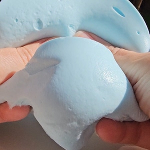 May include: A light blue slime being stretched and pulled apart by two hands.