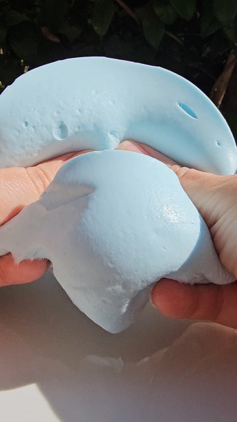 May include: A light blue slime being stretched and pulled apart by two hands.