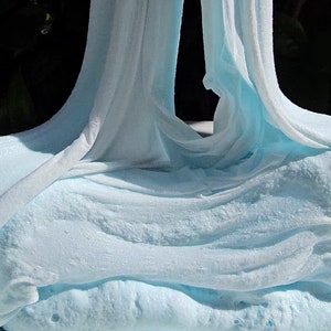 May include: A close-up of light blue slime, stretched and pulled into a long, thin shape. The slime is soft and gooey, with a slightly textured surface.