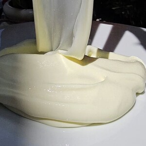 May include: A close-up of a white, creamy substance being poured onto a white plate. The substance is thick and smooth, and it has a slightly glossy finish.