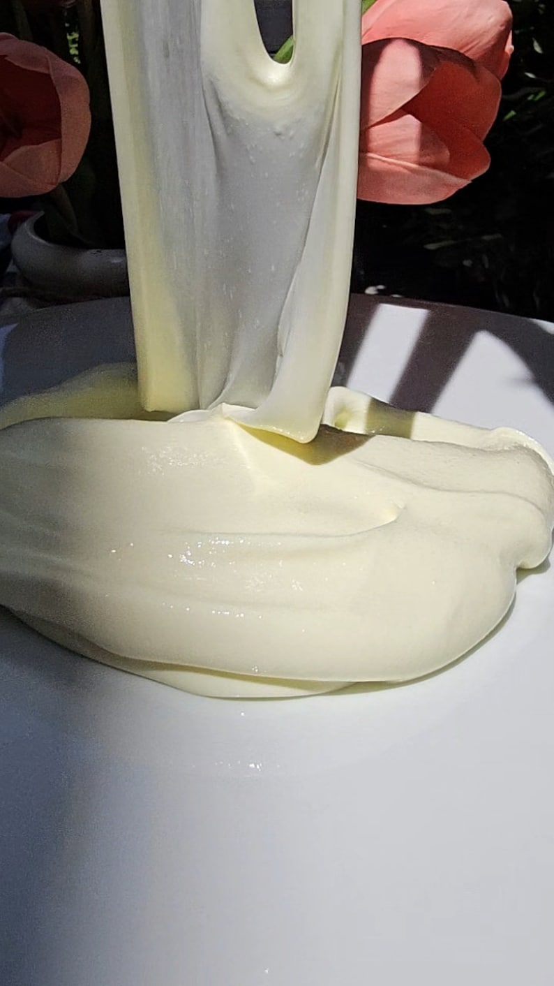 May include: A close-up of a white, creamy substance being poured onto a white plate. The substance is thick and smooth, and it has a slightly glossy finish.