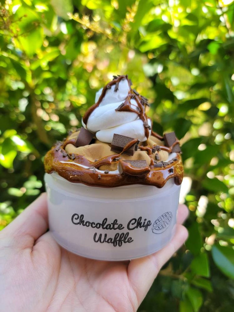 以下が含まれることがあります： チョコレートチップワッフルのスライムが入った白い容器。スライムはホイップクリームとチョコレートソースでトッピングされています。容器には「チョコレートチップワッフル」という文字が印刷されています。
