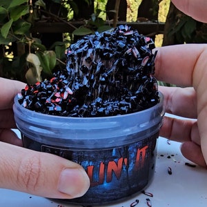 K&ouml;nnte beinhalten: Ein durchsichtiger Plastikbeh&auml;lter gef&uuml;llt mit schwarzem und rotem Schleim mit dem Aufdruck "Slime It" auf der Seite.