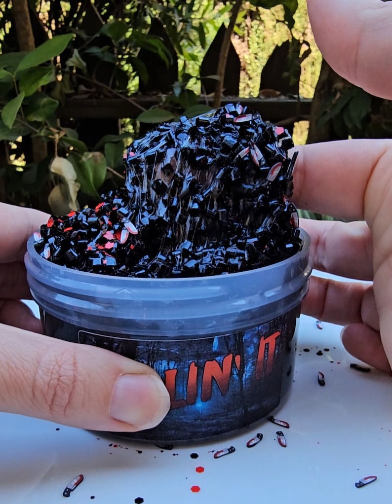 K&ouml;nnte beinhalten: Ein durchsichtiger Plastikbeh&auml;lter gef&uuml;llt mit schwarzem und rotem Schleim mit dem Aufdruck "Slime It" auf der Seite.