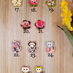 Op de afbeelding: Assortiment van 26 houten knopen met verschillende bloemen- en dierenmotieven. De knopen zijn in tinten roze, groen, blauw, wit en zwart. De knopen zijn genummerd van 17 tot en met 26.