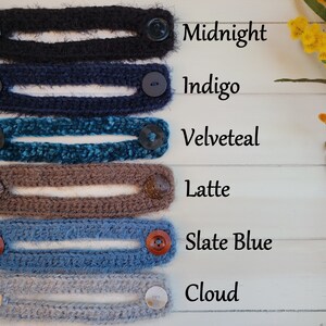 Op de afbeelding: Zes gehaakte oorschoners in verschillende kleuren, waaronder middernacht, indigo, fluweel teal, latte, leisteenblauw en wolk. Elke oorschoner heeft twee knopen aan de uiteinden.