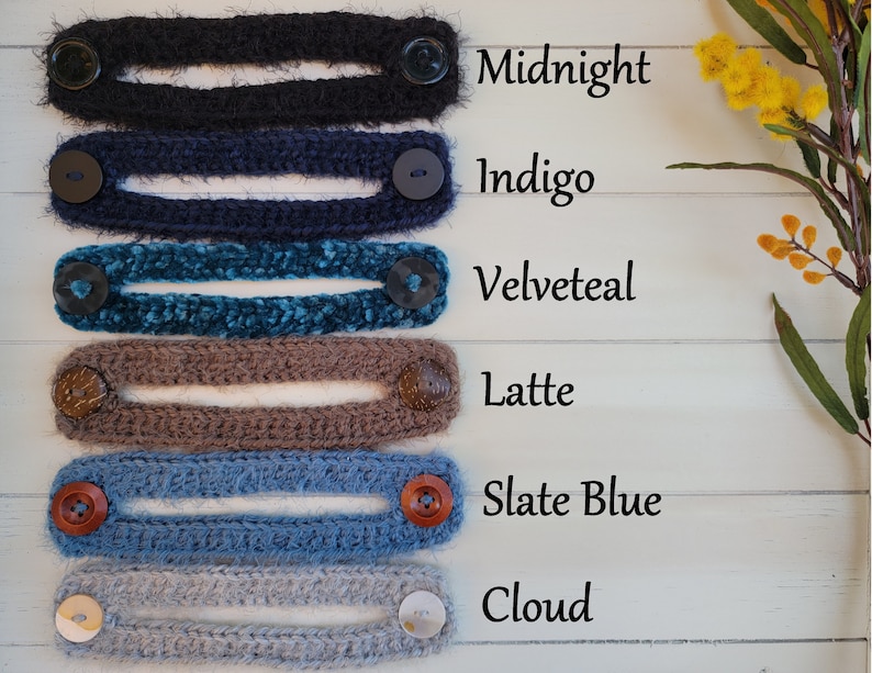 Op de afbeelding: Zes gehaakte oorschoners in verschillende kleuren, waaronder middernacht, indigo, fluweel teal, latte, leisteenblauw en wolk. Elke oorschoner heeft twee knopen aan de uiteinden.