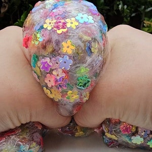 May include: A clear slime with iridescent flower-shaped glitter embedded throughout. The slime is being held in two hands.
