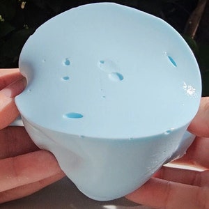 May include: A light blue silicone mold with a smooth surface and several small holes. The mold is shaped like a heart with a rounded top.
