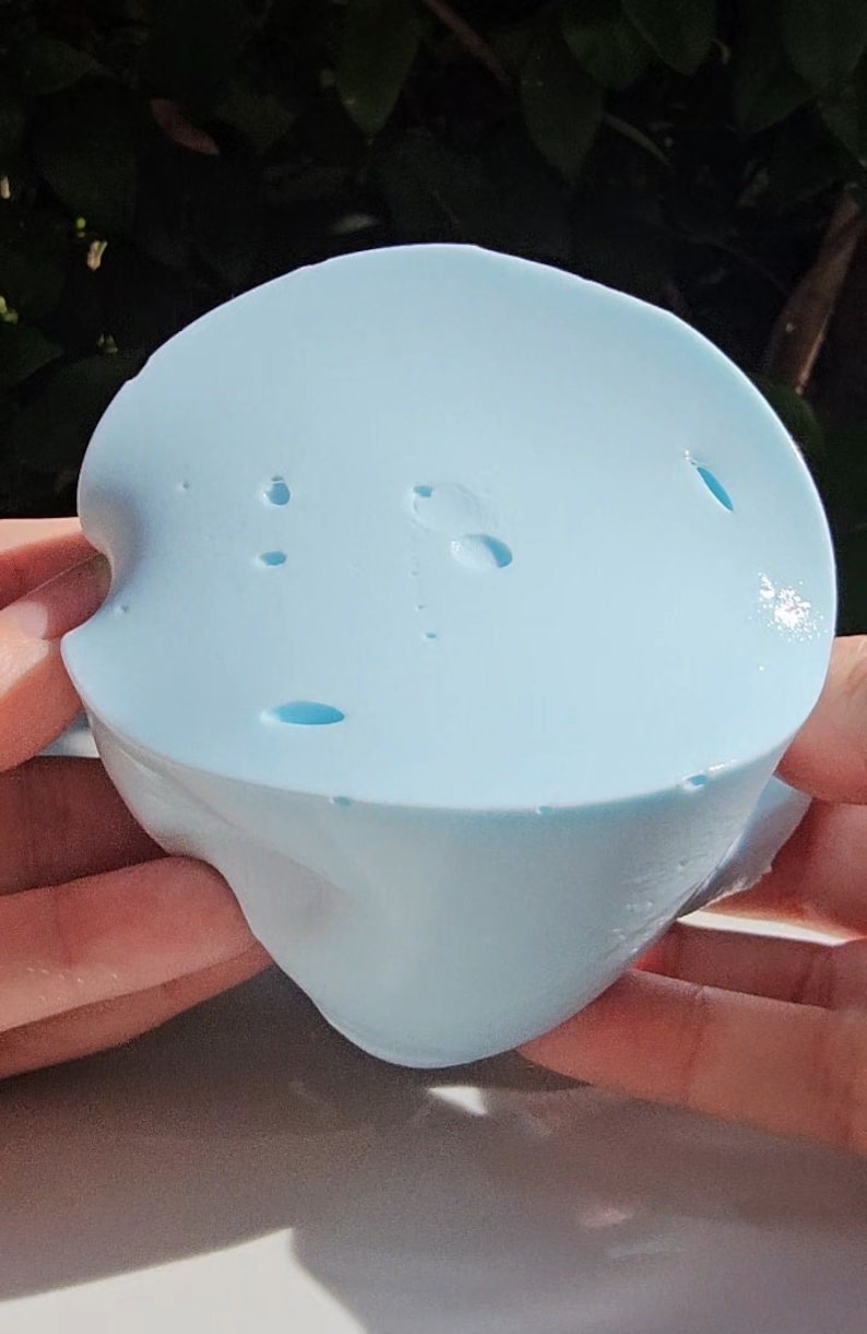 May include: A light blue silicone mold with a smooth surface and several small holes. The mold is shaped like a heart with a rounded top.