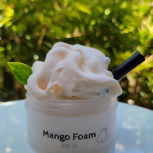 K&ouml;nnte beinhalten: Ein durchsichtiger Plastikbecher mit einem wei&szlig;en Deckel und einem wei&szlig;en Etikett mit der Aufschrift "Mango Foam Boba Tea". Der Becher ist mit einem hellrosa, geschlagenen Mangoschaum gef&uuml;llt. Ein schwarzer Strohhalm ragt aus dem Schaum.
