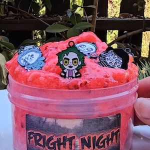 May include: A red slime with a black and white label that says "FRIGHT NIGHT". The slime has several small charms in it, including a cartoon character with green hair and a black and white face.