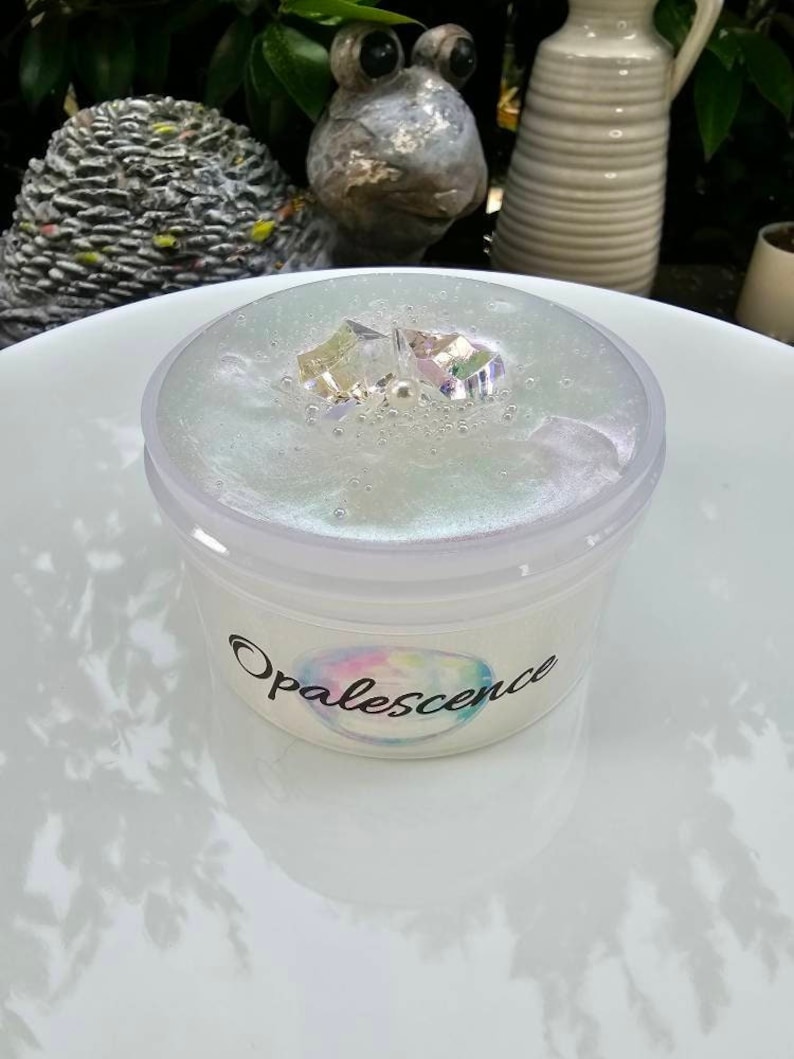 Op de afbeelding: Een doorzichtige slijmbeker met iriserende glitter en een wit label met de tekst "Opalescence".