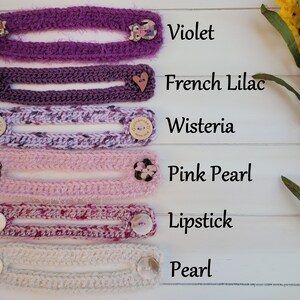 Op de afbeelding: Zes gehaakte maskerverlengers in verschillende tinten paars, roze en wit. De verlengers zijn gelabeld met de kleuren: Violet, Frans Lila, Wisteria, Roze Parel, Lipstick en Parel.