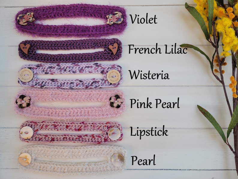 Op de afbeelding: Zes gehaakte maskerverlengers in verschillende tinten paars, roze en wit. De verlengers zijn gelabeld met de kleuren: Violet, Frans Lila, Wisteria, Roze Parel, Lipstick en Parel.