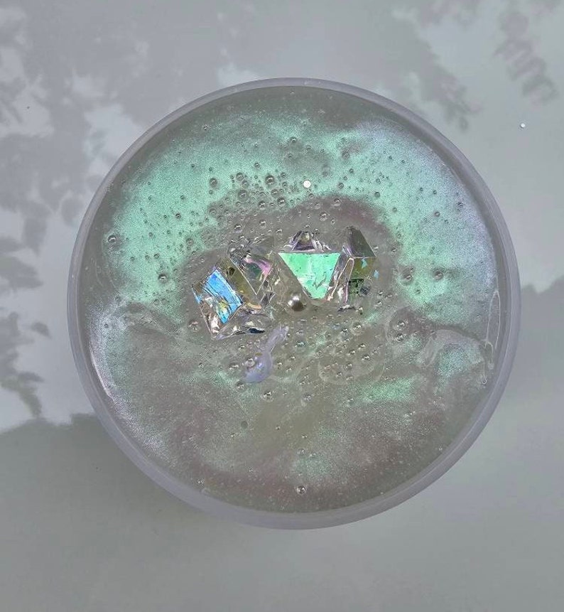 Op de afbeelding: Een heldere, iriserende slijm met een groene tint en een paar luchtbellen. Drie iriserende, gefacetteerde kristallen zijn ingebed in de slijm.
