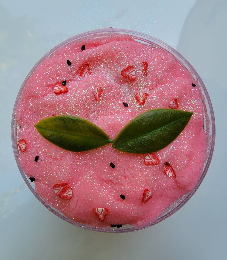 Peut inclure: Slime rose avec des paillettes et des graines noires, surmont&eacute; de feuilles vertes et de p&eacute;pites rouges en forme de c&oelig;ur.